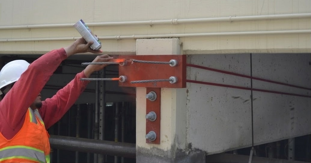 Worker marking external post-tensioning tendons anchored to a concrete beam during a post tension slab strengthening repair