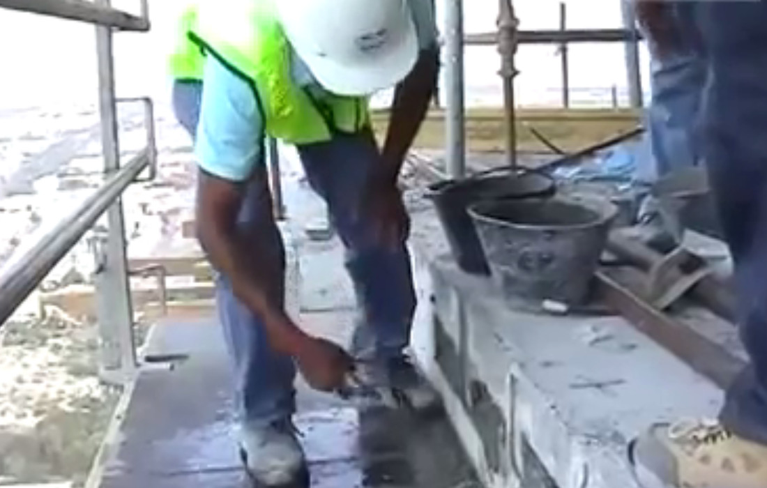Worker filling a stressed live-end anchor pocket with grout at the edge of a post tension slab