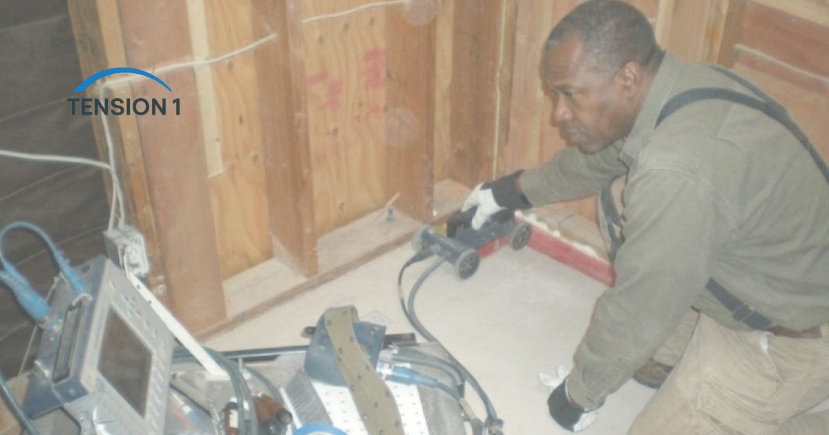 Technician scanning a post tension slab with a ground-penetrating radar cart inside a framed house to locate tendons before any cutting
