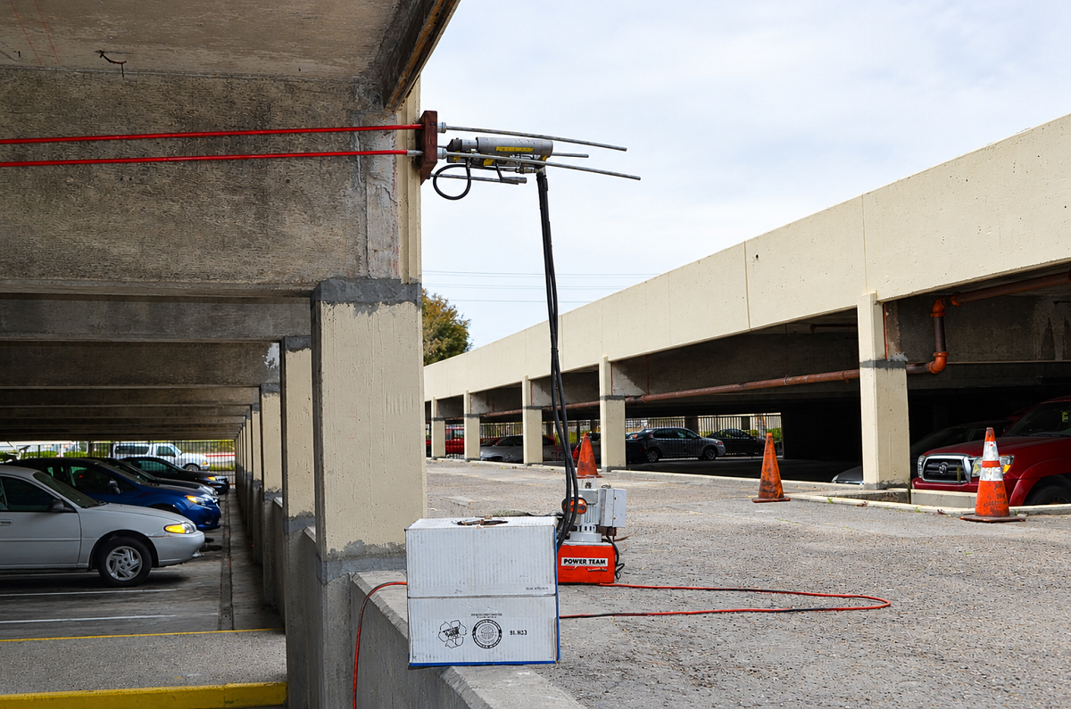 Monostrand stressing jack mounted at the edge of a post tension slab in a parking garage, connected by hydraulic hose to a stressing pump for a tendon repair